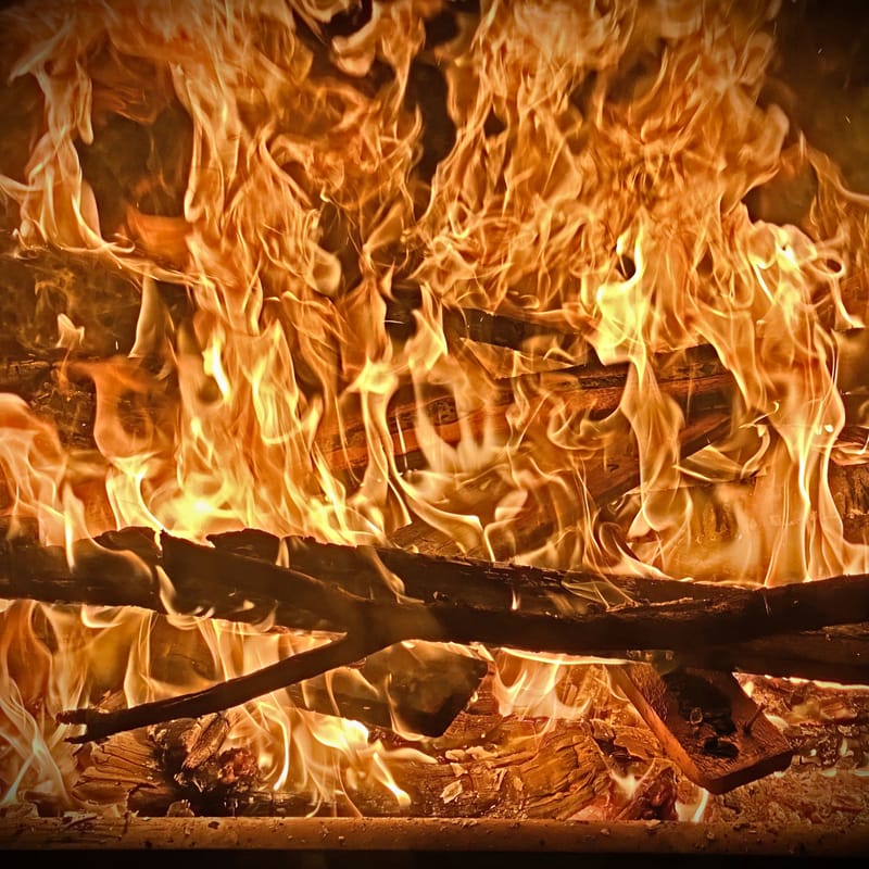 Roaring orange flames engulf crossed logs in a dark fireplace, deep amber glow