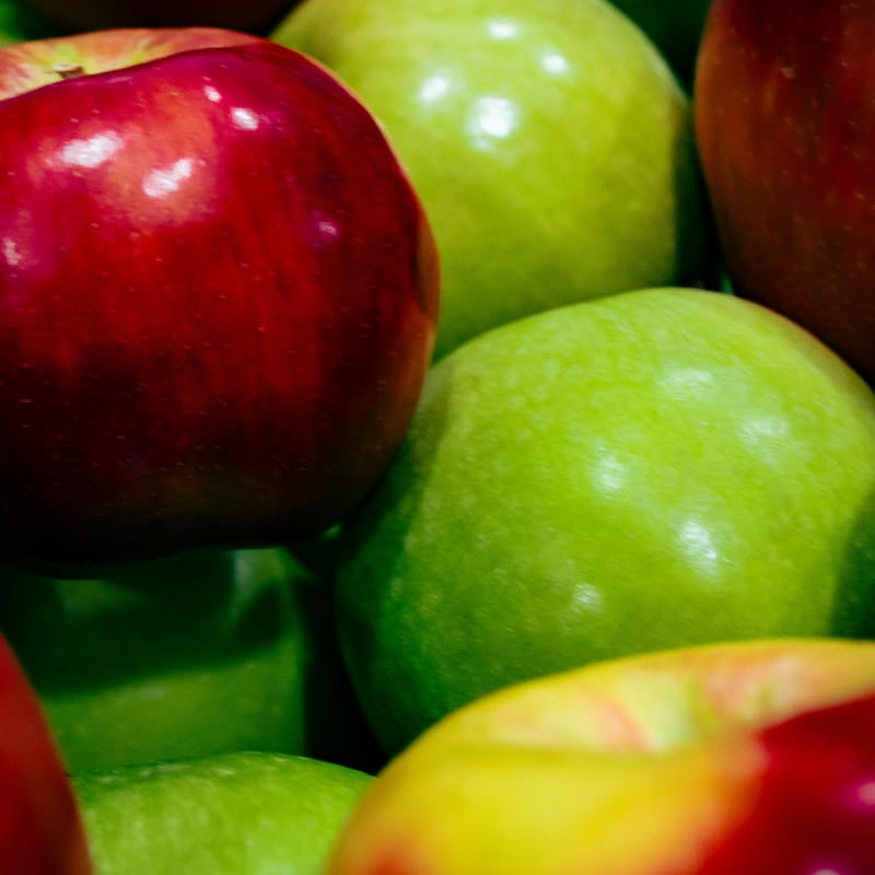 Glossy red and green apples piled close together, catching bright highlights
