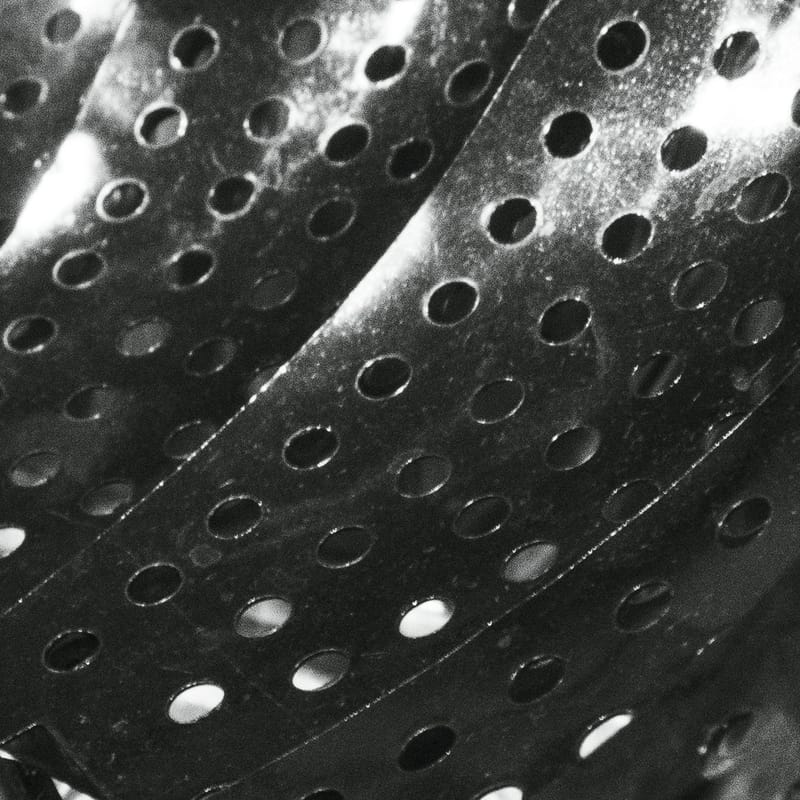 Rows of round perforations in brushed metal panels, angled with soft light