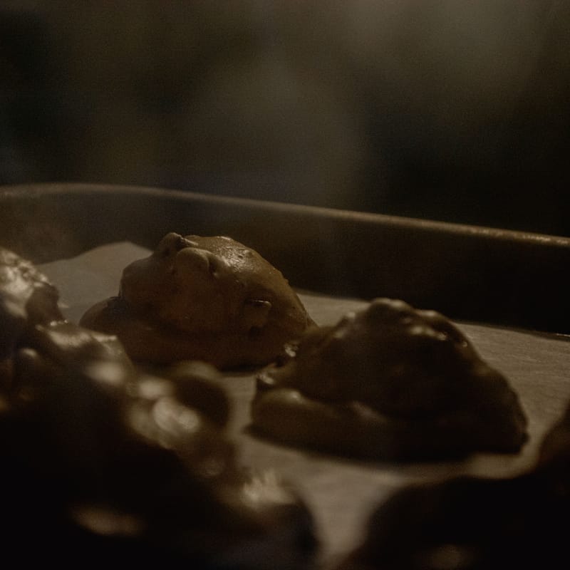 Three lumps of raw cookie dough on a baking sheet, dim warm kitchen light