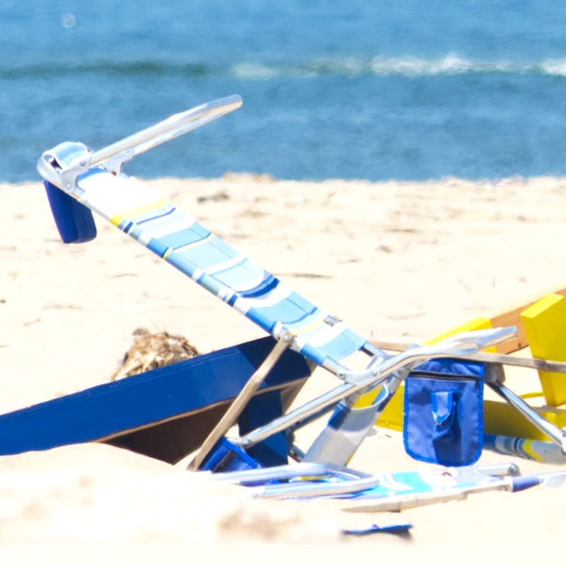 Blue-striped beach chairs and boogie boards planted in sand, a boat passing offshore