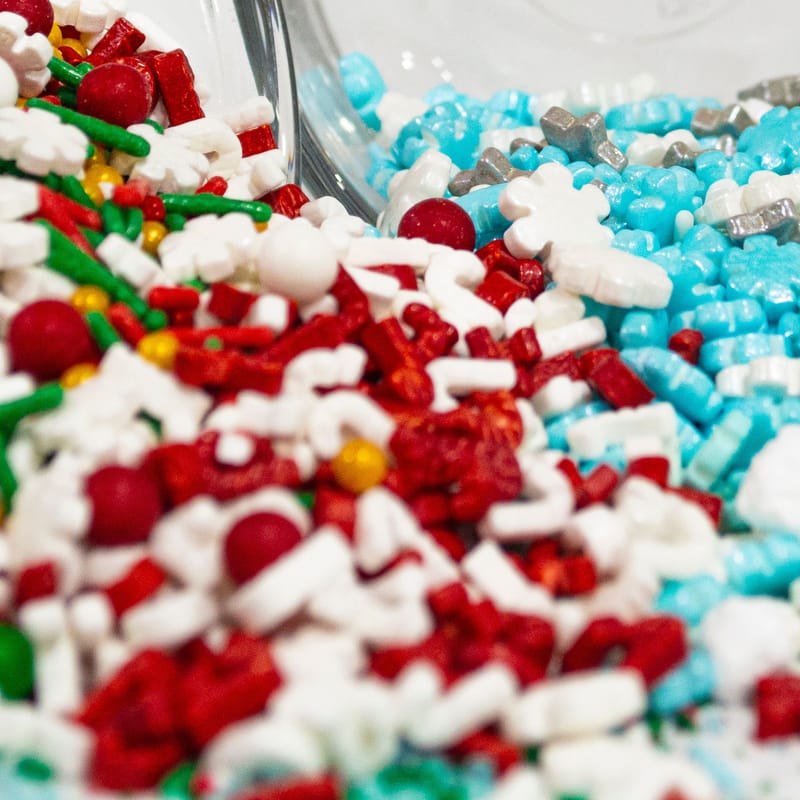 Close-up of red, blue, and white candy sprinkles spilling into a mound of powdered sugar