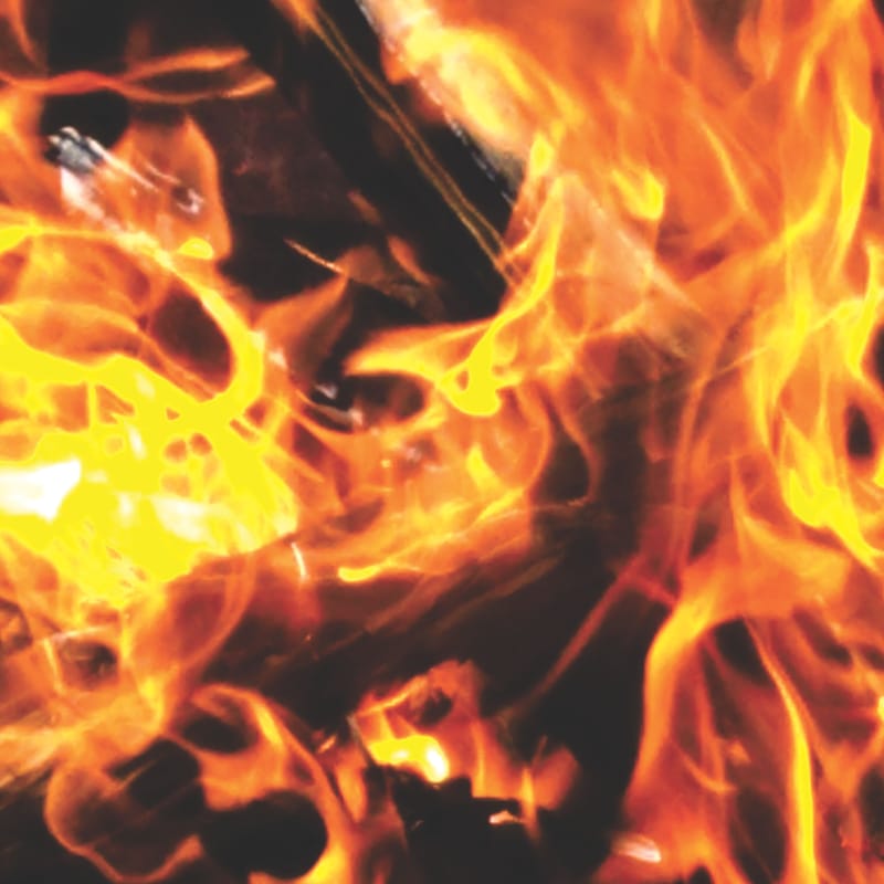 Close-up of bright orange and yellow flames licking over dark charred wood