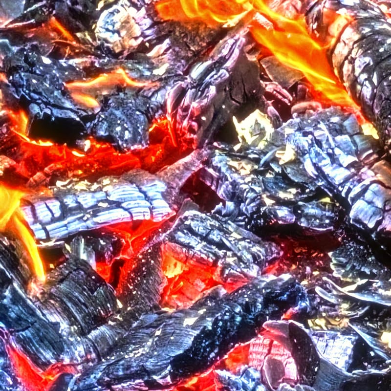 Macro of deep red glowing coals amid blackened charcoal in a fire pit