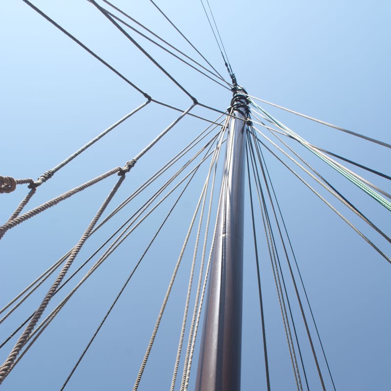 Sailboat mast and rigging lines fanning outward against a clear blue sky, viewed from below