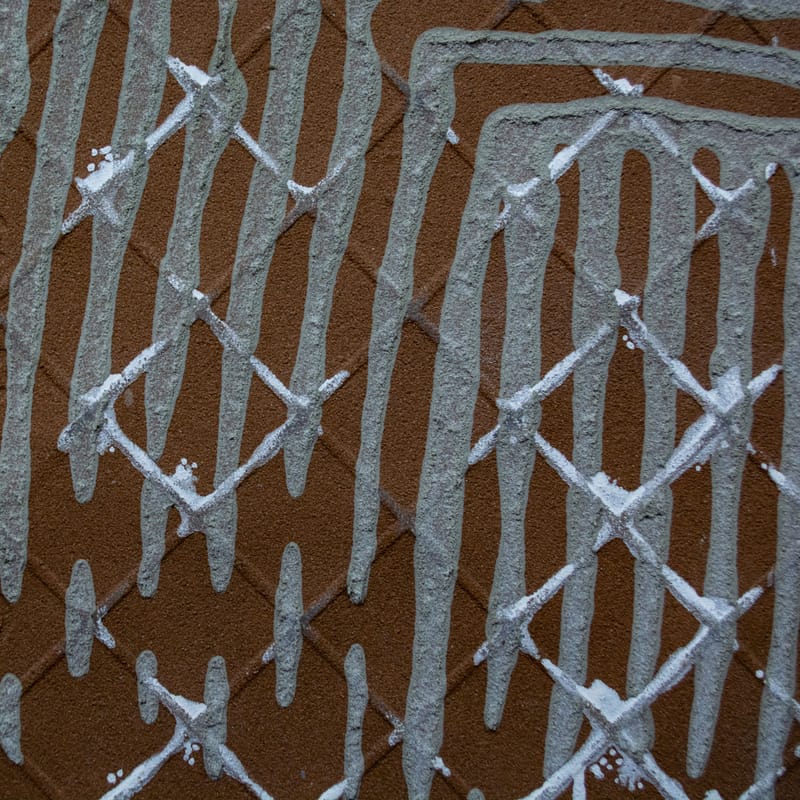 Close-up of white paint dripping in an X-lattice pattern over brown stucco wall