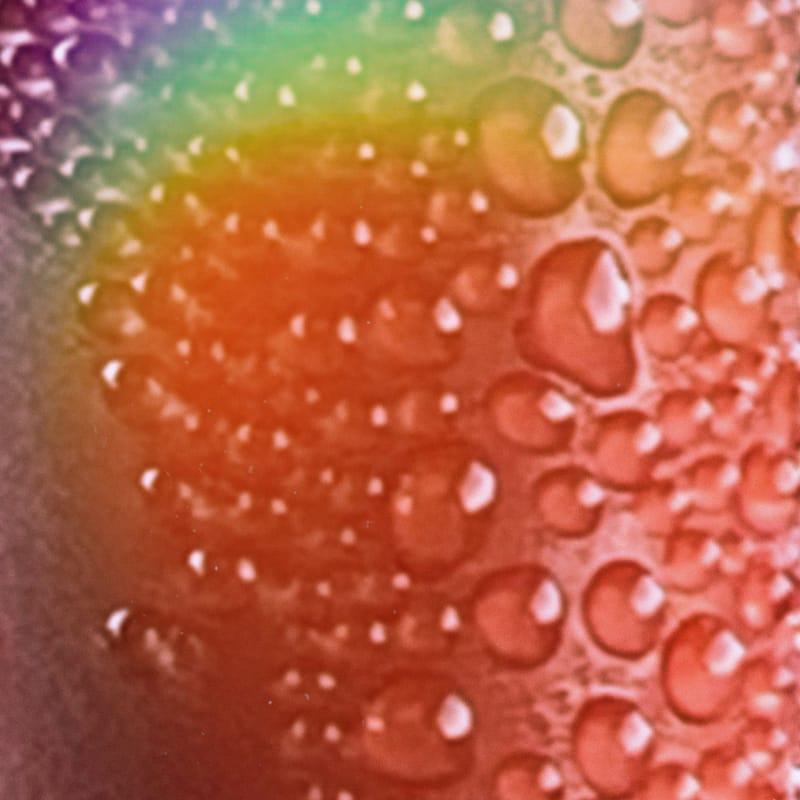 Macro water droplets on orange surface with a rainbow light flare across corner