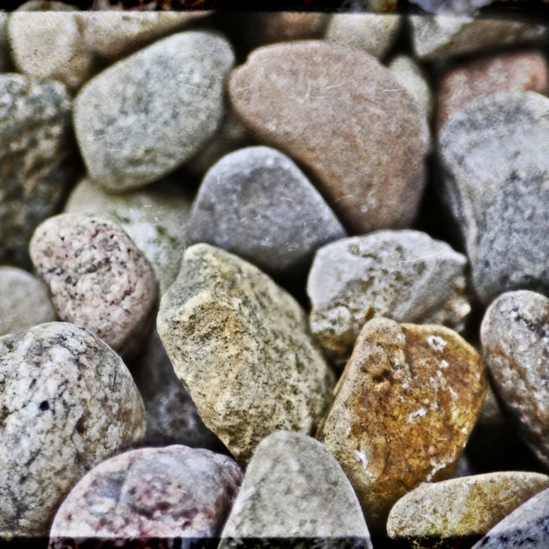 Close-up of smooth river rocks in muted earth tones, vignette-framed macro