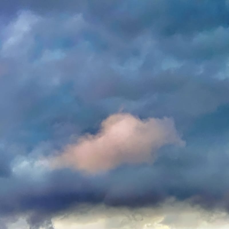 Layered storm clouds in blue-gray tones with a soft peach-pink glow breaking through