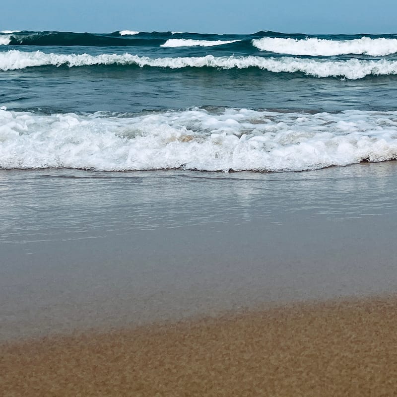 White foam waves roll onto wet tan sand under a hazy blue sky